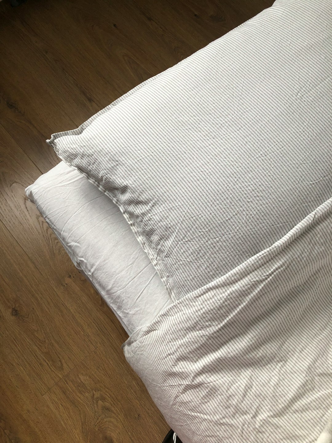 A bed covered with white and striped bed linen, a striped pillow is visible lying on the bed